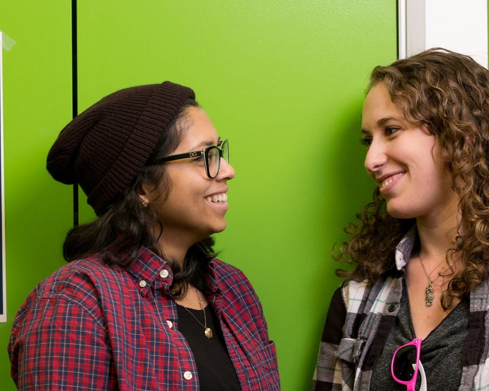 Two female teens beside a YouthCan IMPACT poster