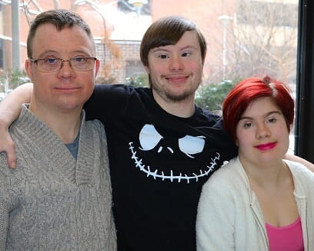 Two men and a woman with Down Syndrome smiling. 