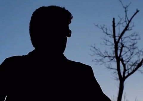 A black shadow of a person with glasses on a gradient blue background with a tree on the right. 