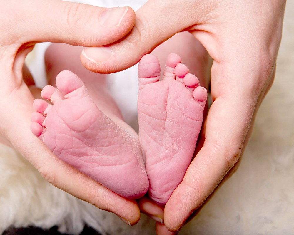 Adult hands form a heart around baby's feet.