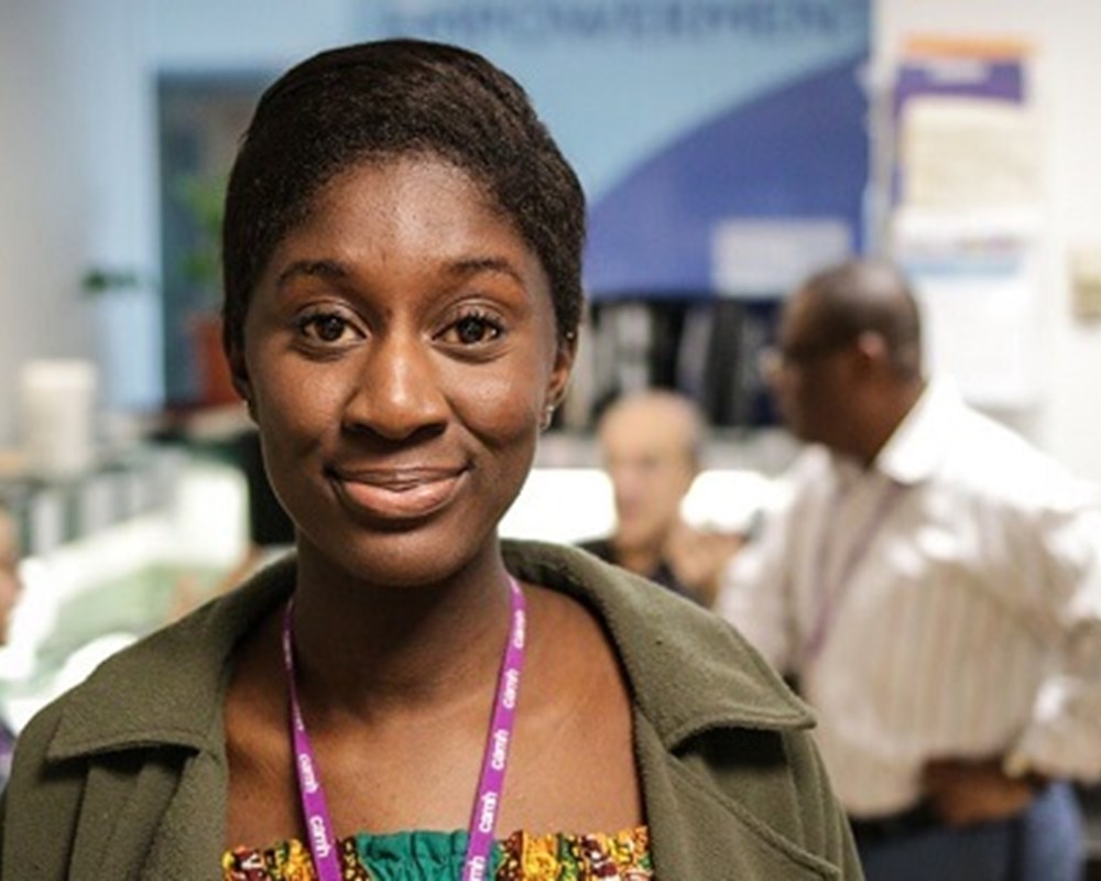 A female CAMH staff of colour wearing a forest green cardigan, posing for a picture in one of the nursing stations. 