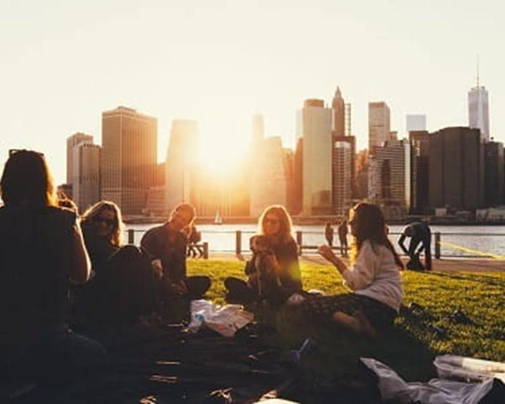 A group of women having a picnic in a park with the city line and sunset behind them. 