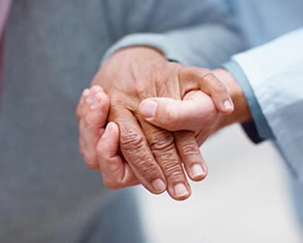 A doctor's hand supporting an elderly person by holding onto the person's hand. 