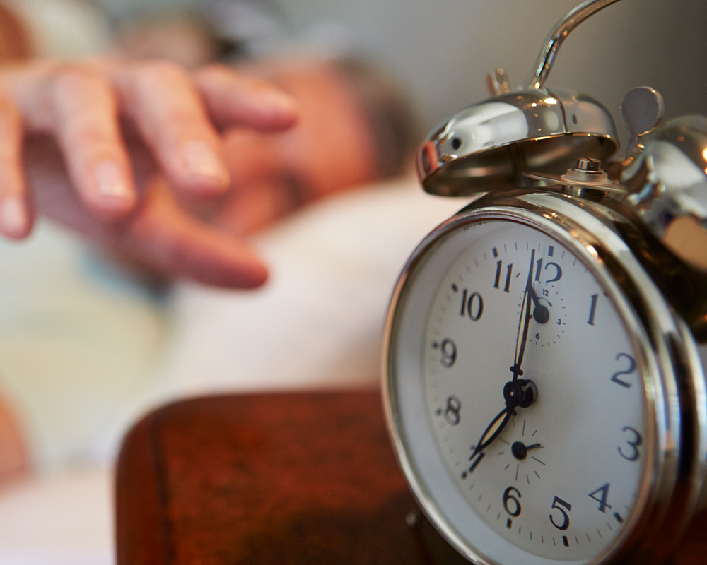 man in bed reaching for alarm clock