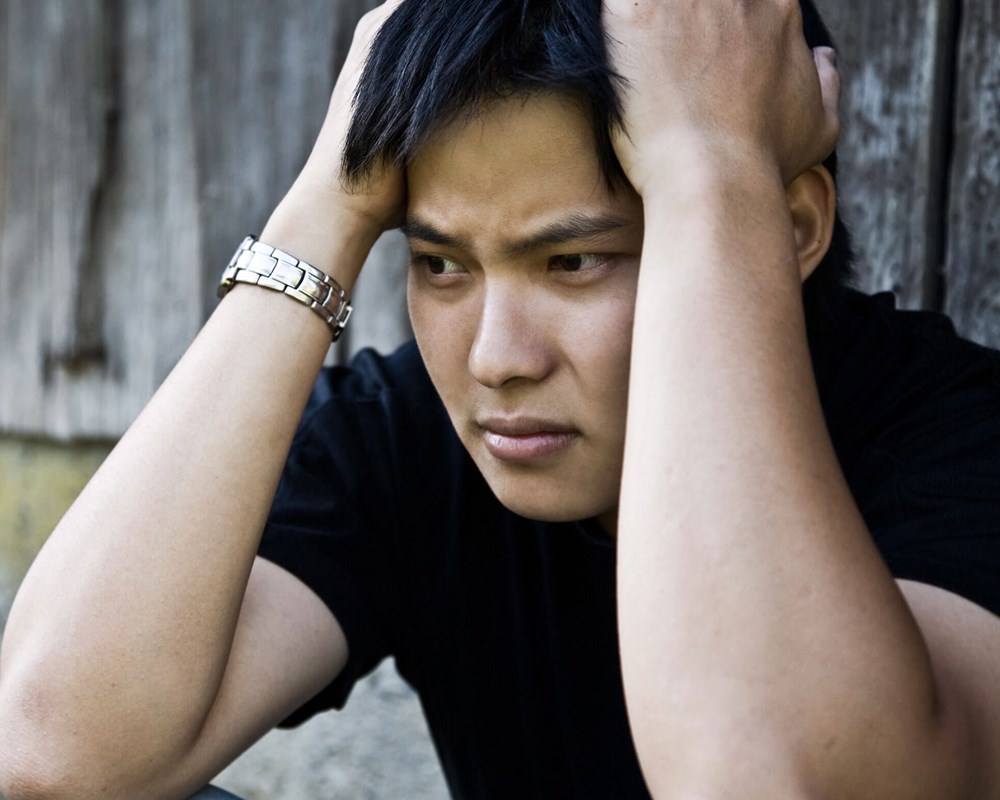 Young Asian man holding his head, looking sad.
