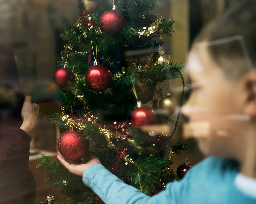 Woman watched child decorating a Christmas tree through a window.