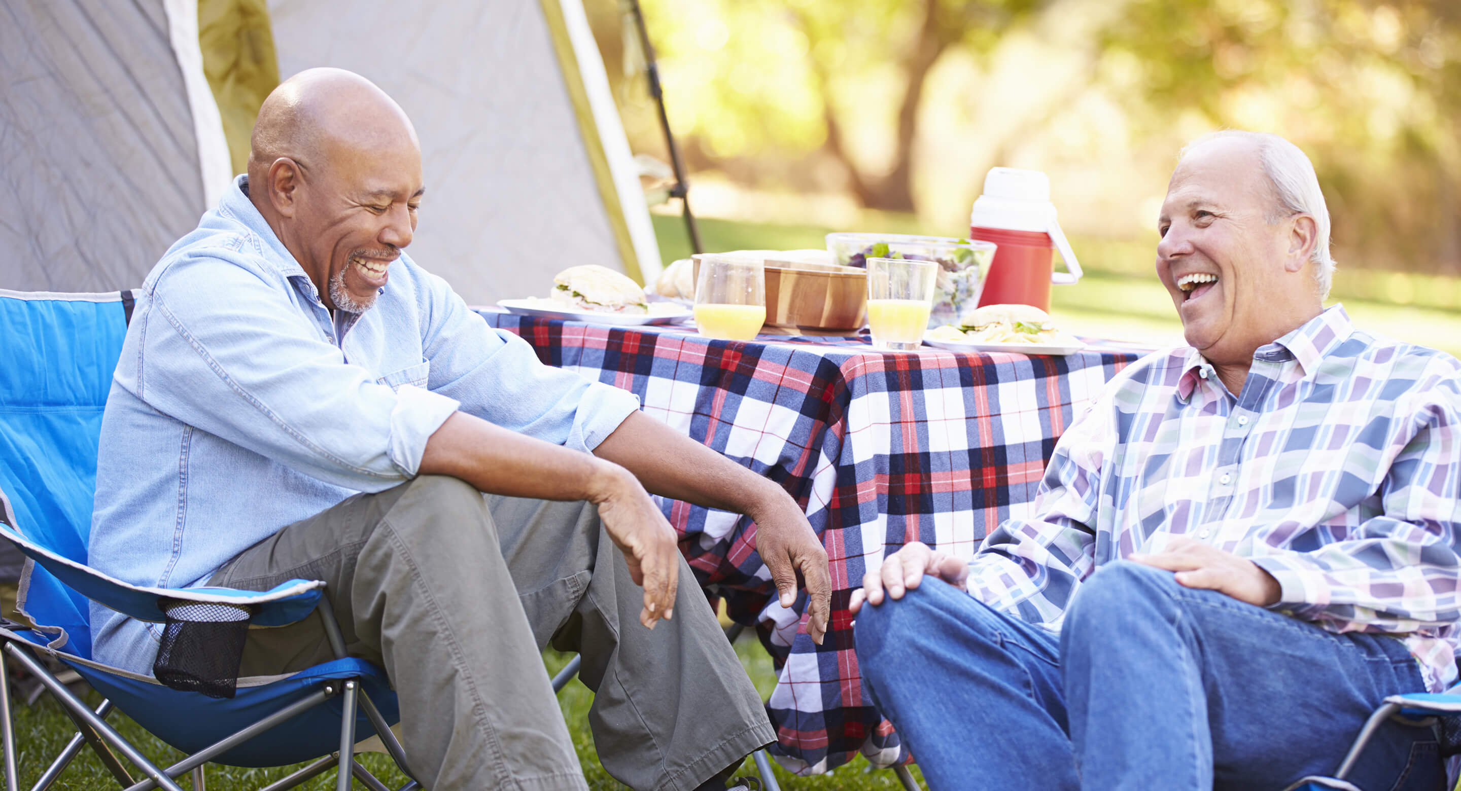 Two older men laughing and talking at a campsite