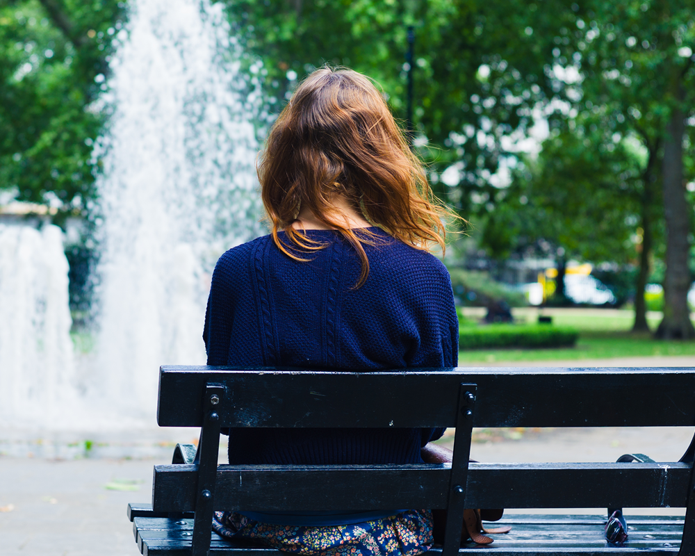 young woman sitting on bench facing away