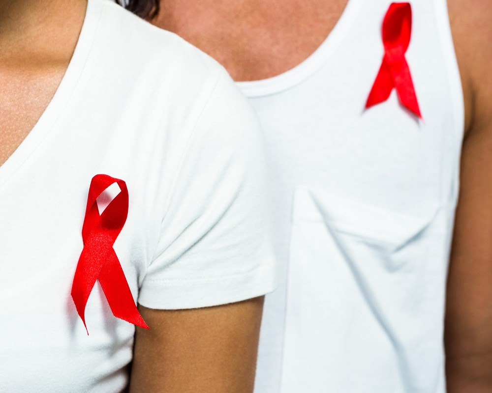 Close up image of two adults wearing red ribbons for AIDS awareness.