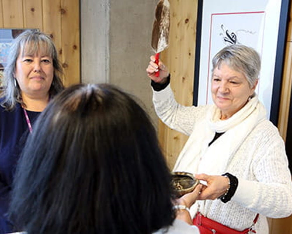 Aboriginal Service client Flo at a prayer circle smudge ceremony with social worker Barbara Hurford (holding the feather) and CAMH Elder Diane Longboat.
