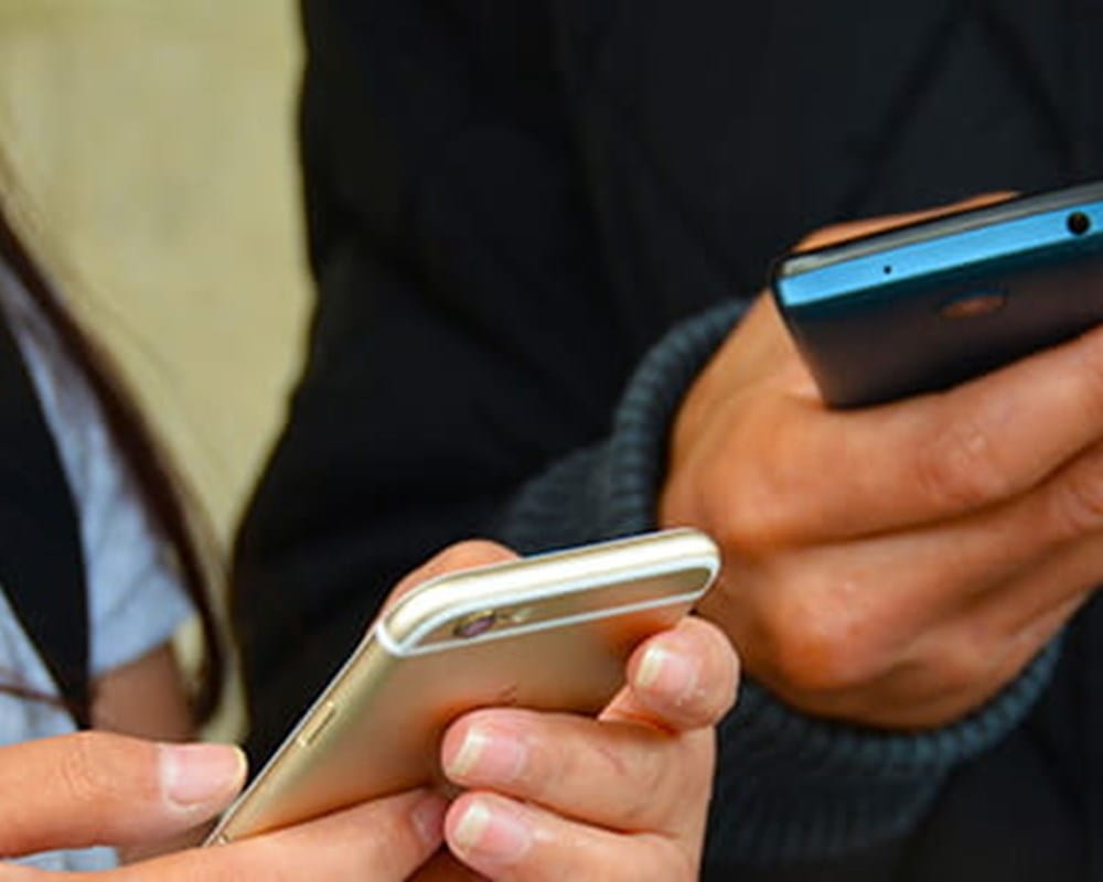 A close-up of two individuals texting one their cellphones. 