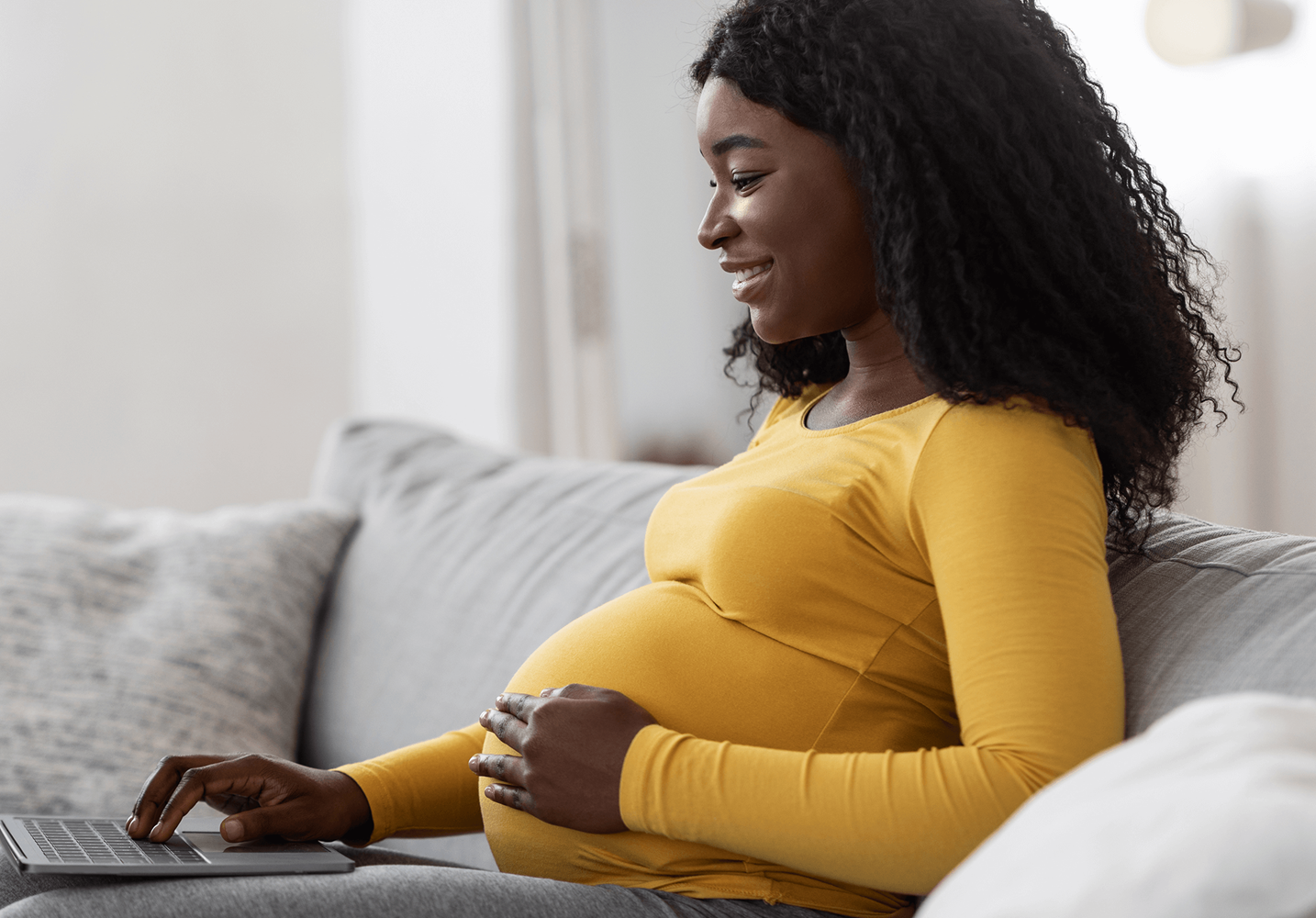 Black pregnant woman using laptop at home.