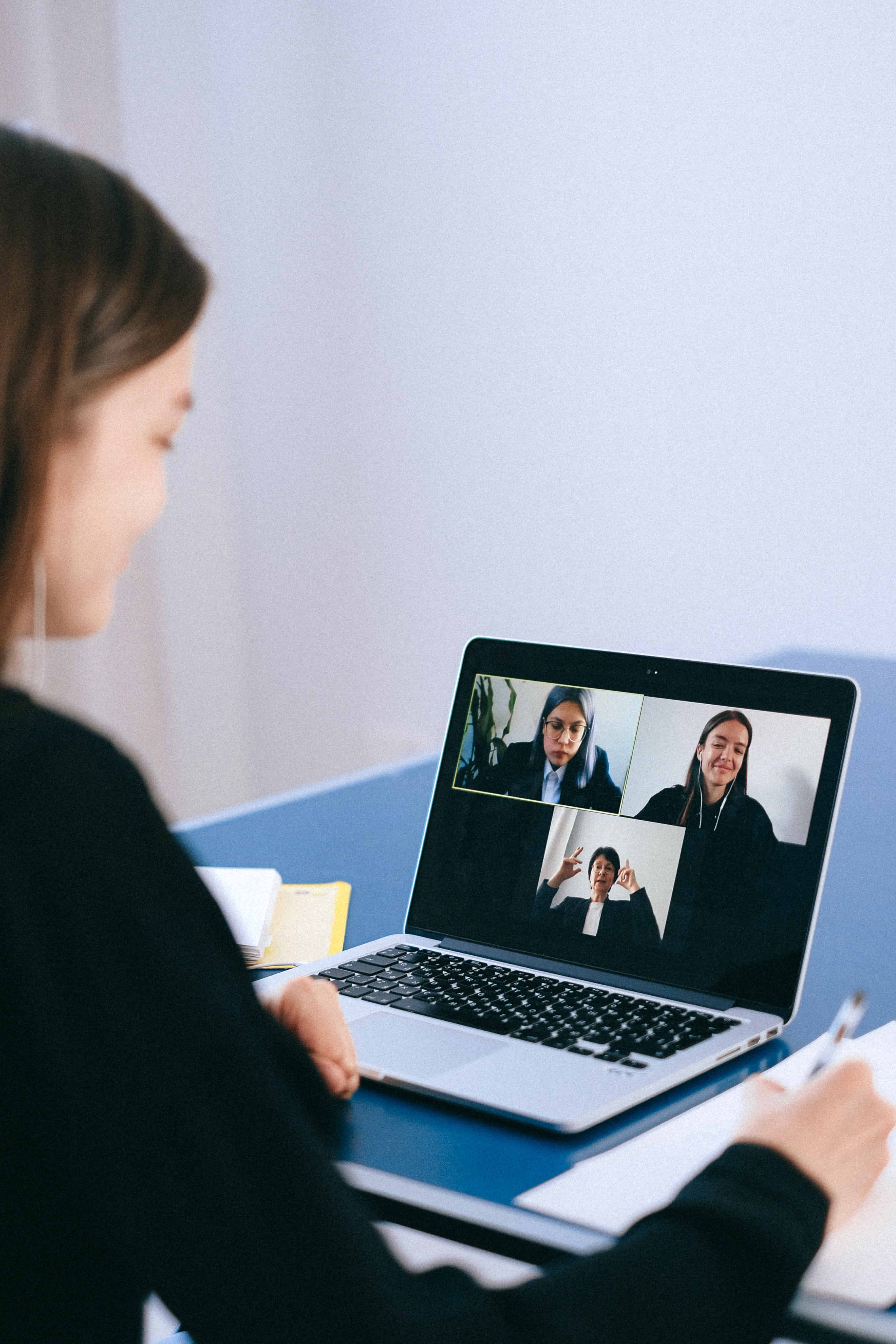 Woman in video call meeting, looking at a computer screen showing three other women.